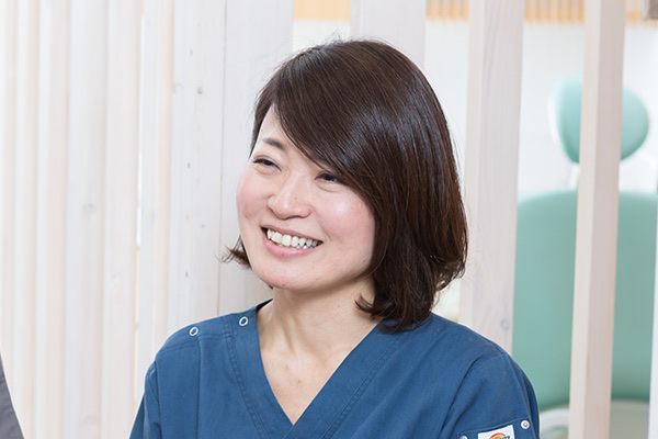 木の格子が並ぶ診療室で笑顔を見せる歯科医師の岡本千穂