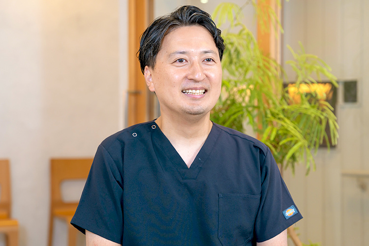 紺色のスクラブを着て笑顔で話す院長の全並匠