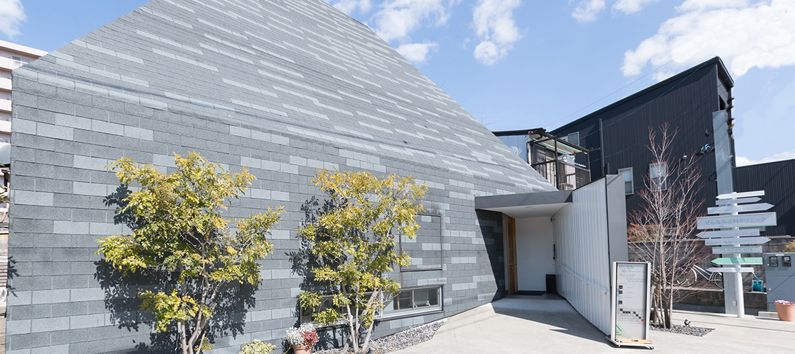 三角屋根とグレーの石張り壁が特徴的なぜんなみ歯科クリニックの外観